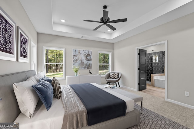 carpeted bedroom featuring multiple windows, connected bathroom, a raised ceiling, and ceiling fan