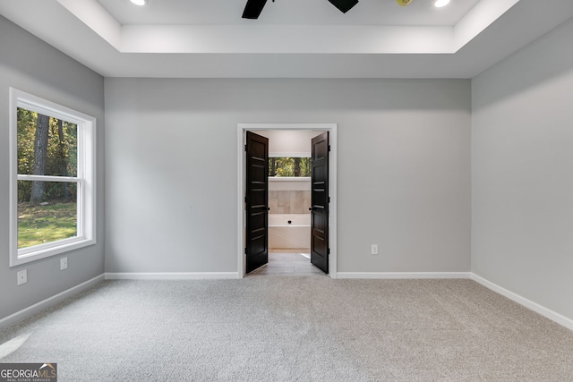 empty room featuring light carpet, a tray ceiling, and ceiling fan