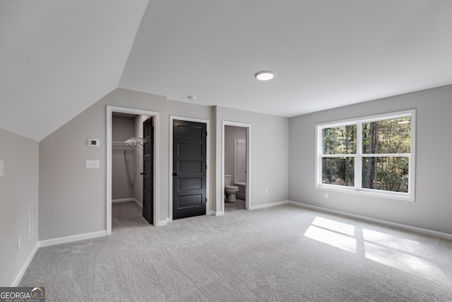 unfurnished bedroom with a walk in closet, light colored carpet, and ensuite bath