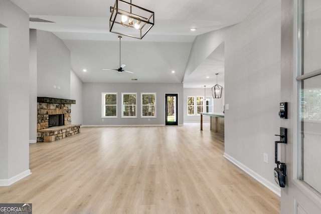 living room featuring a stone fireplace, high vaulted ceiling, ceiling fan with notable chandelier, and light wood-type flooring