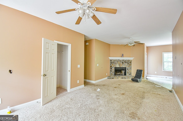 unfurnished living room featuring a stone fireplace, light colored carpet, and ceiling fan