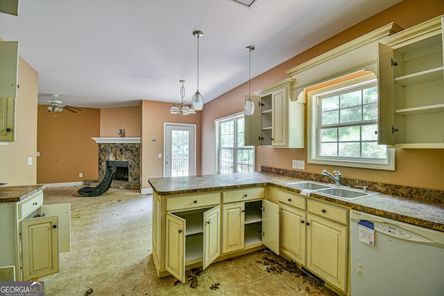 kitchen with kitchen peninsula, ceiling fan with notable chandelier, dishwasher, a stone fireplace, and sink