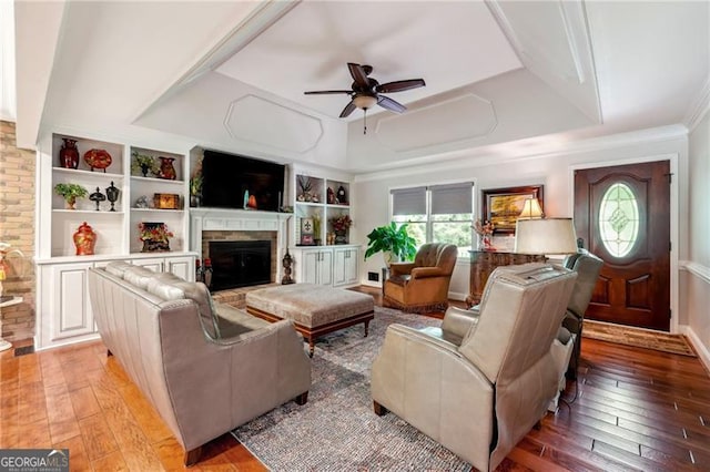 living room featuring ceiling fan, light hardwood / wood-style floors, a tray ceiling, and ornamental molding