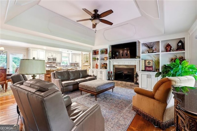 living room with ceiling fan, a brick fireplace, hardwood / wood-style flooring, and a raised ceiling