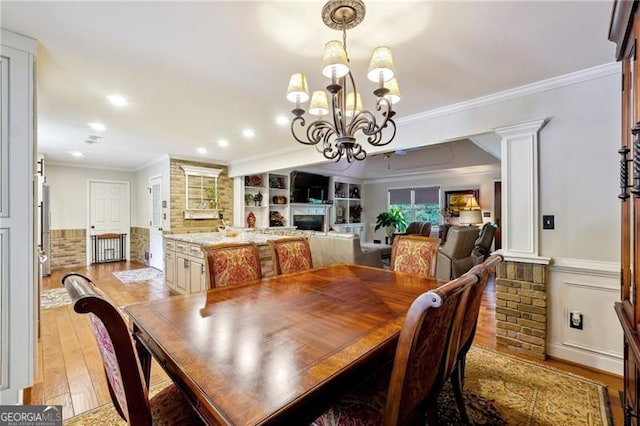 dining room featuring built in shelves, a notable chandelier, ornamental molding, and light hardwood / wood-style floors