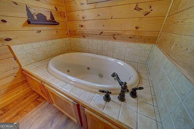 bathroom with wood walls, hardwood / wood-style floors, and a bath