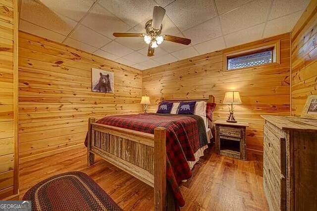 bedroom with wood walls, wood-type flooring, and a paneled ceiling