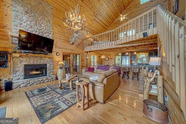 living room with wood walls, high vaulted ceiling, light hardwood / wood-style floors, a stone fireplace, and wood ceiling