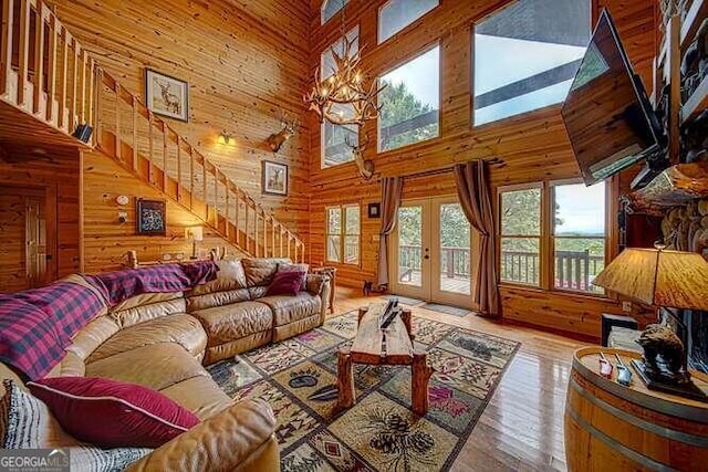 living room with wood walls, light wood-type flooring, french doors, and high vaulted ceiling