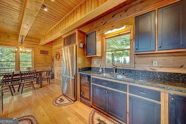 kitchen featuring stainless steel refrigerator, light wood-type flooring, wood walls, pendant lighting, and sink