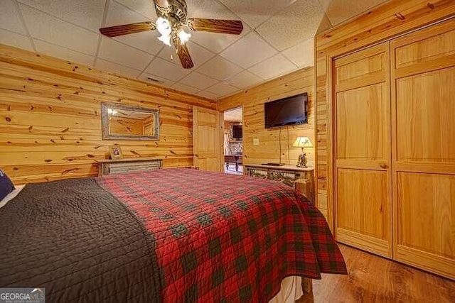 bedroom with light hardwood / wood-style floors, wooden walls, ceiling fan, and a drop ceiling