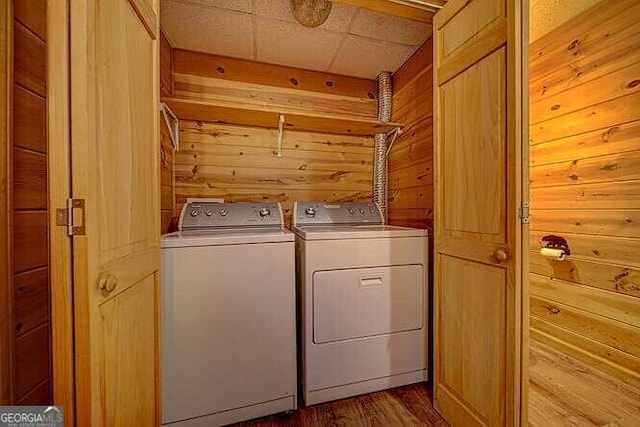 laundry room featuring wood-type flooring, wood walls, and washer and dryer