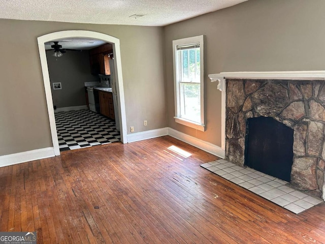 unfurnished living room with a textured ceiling, light hardwood / wood-style flooring, ceiling fan, and a stone fireplace