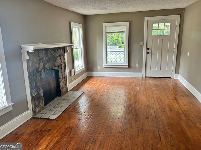 entrance foyer featuring wood-type flooring, a textured ceiling, and a stone fireplace