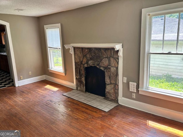 unfurnished living room featuring a textured ceiling, a healthy amount of sunlight, wood-type flooring, and a stone fireplace