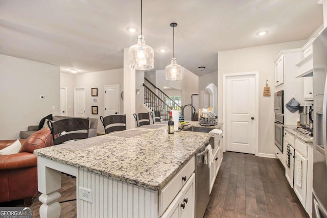 kitchen featuring a kitchen bar, white cabinetry, appliances with stainless steel finishes, pendant lighting, and a kitchen island with sink