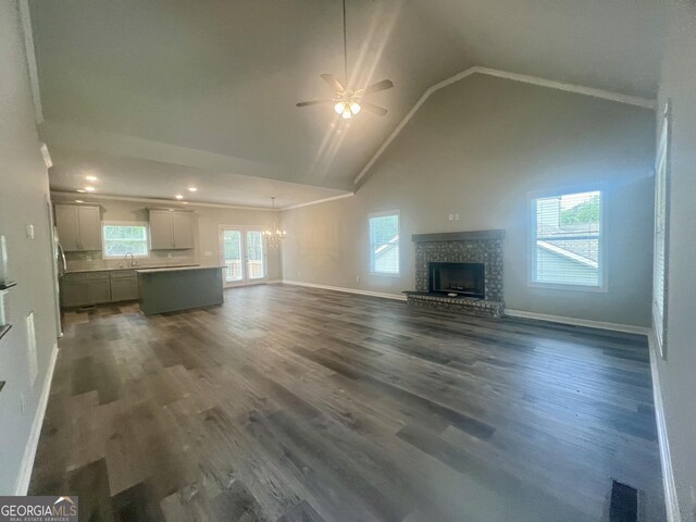 unfurnished living room featuring high vaulted ceiling, a brick fireplace, hardwood / wood-style flooring, and ceiling fan with notable chandelier