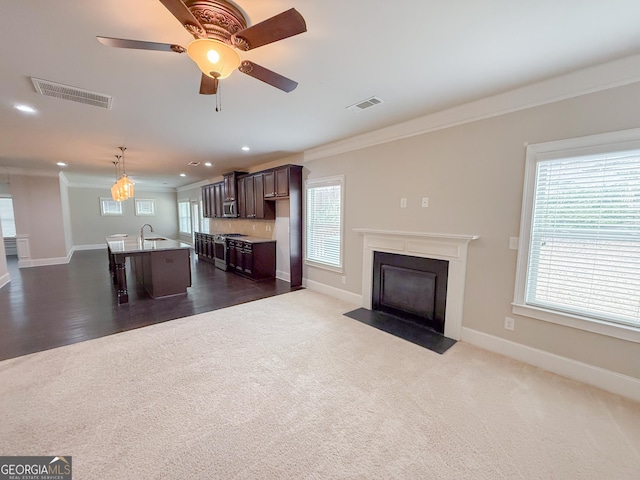 unfurnished living room featuring ornamental molding, sink, ceiling fan, and dark carpet