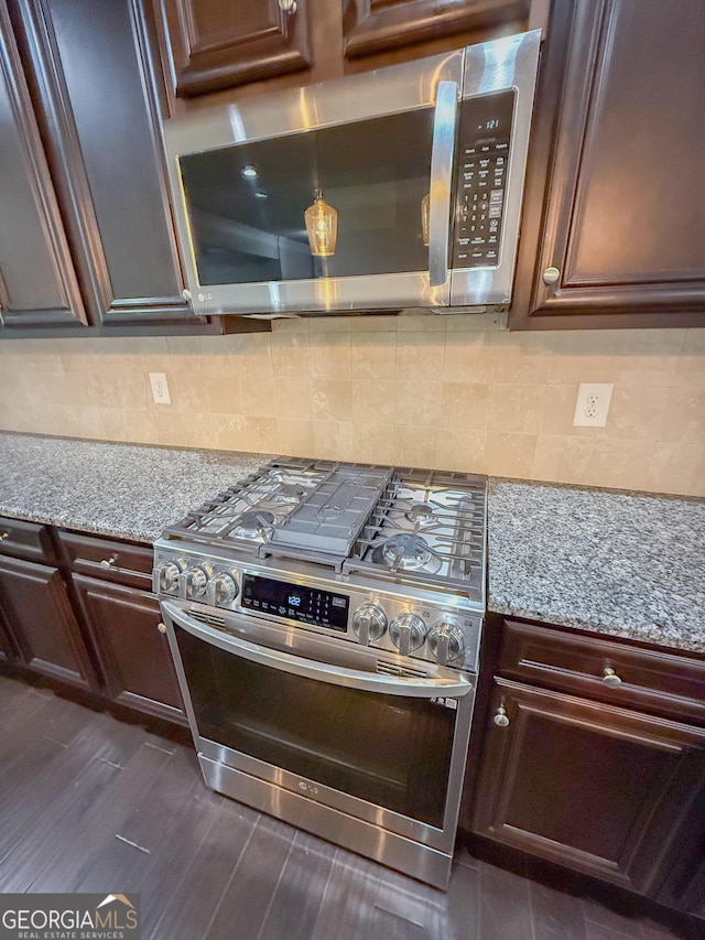 kitchen featuring stainless steel appliances, dark hardwood / wood-style floors, light stone countertops, and backsplash