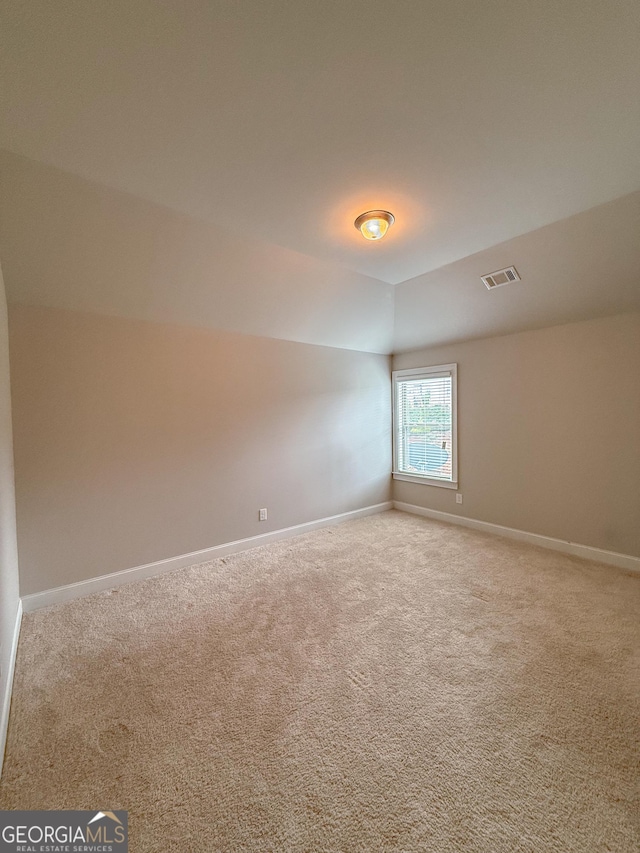 unfurnished room with light colored carpet and vaulted ceiling