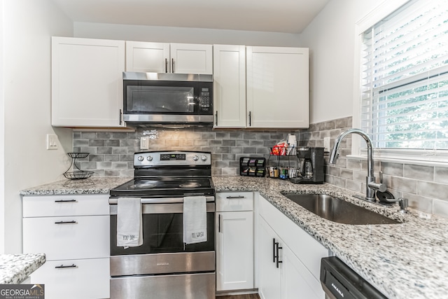 kitchen with white cabinets, backsplash, light stone counters, appliances with stainless steel finishes, and sink