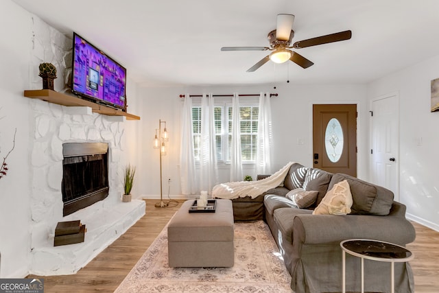 living room featuring a stone fireplace, light wood-type flooring, and ceiling fan