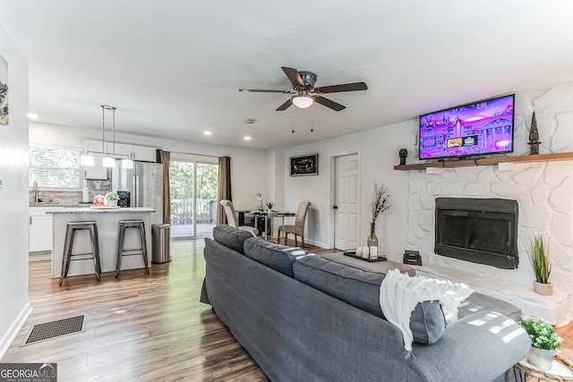 living room featuring light hardwood / wood-style floors, a stone fireplace, ceiling fan, and sink