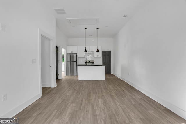 kitchen with a kitchen island, light hardwood / wood-style flooring, decorative light fixtures, white cabinetry, and stainless steel refrigerator