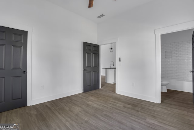 unfurnished bedroom with ensuite bathroom, dark wood-type flooring, and ceiling fan