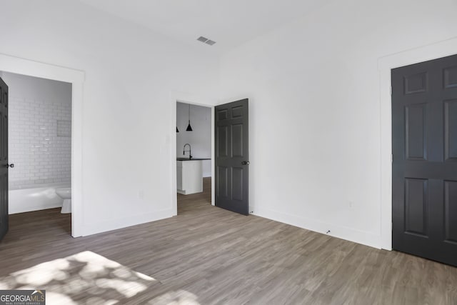 unfurnished bedroom featuring hardwood / wood-style floors, sink, and connected bathroom