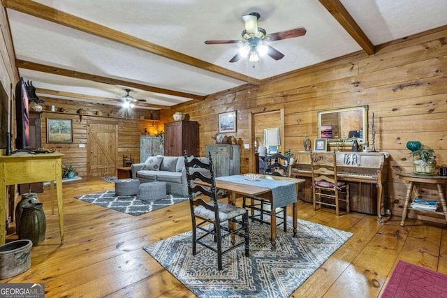 dining room with light wood-type flooring, wooden walls, ceiling fan, and beam ceiling