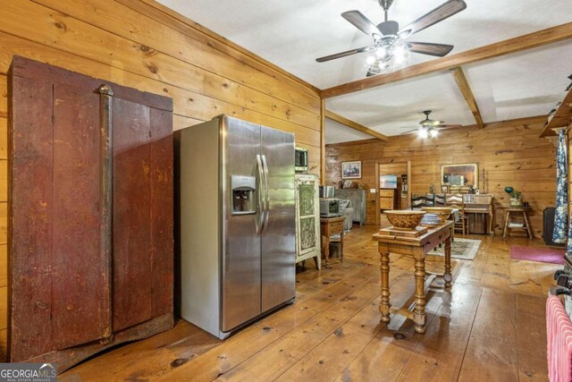 kitchen with stainless steel appliances, wood-type flooring, wooden walls, beamed ceiling, and ceiling fan