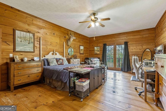 bedroom with wood walls, ceiling fan, a textured ceiling, and light wood-type flooring