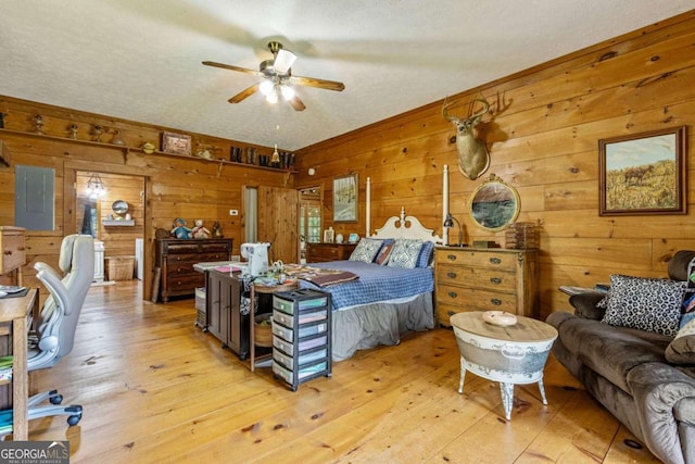 bedroom with light hardwood / wood-style flooring, wooden walls, and ceiling fan