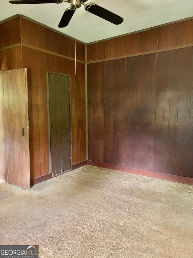 carpeted empty room featuring wood walls and ceiling fan