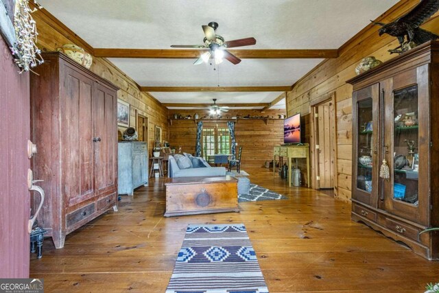 interior space featuring hardwood / wood-style floors, wood walls, ceiling fan, and beam ceiling