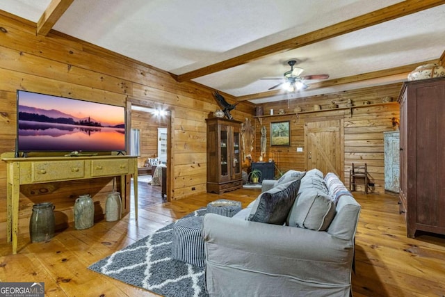 living room featuring a wood stove, light wood-type flooring, ceiling fan, and beam ceiling