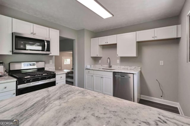 kitchen featuring appliances with stainless steel finishes, sink, white cabinets, light stone counters, and dark hardwood / wood-style floors