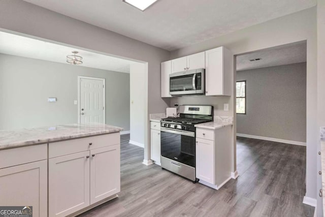 kitchen featuring light stone counters, white cabinets, light hardwood / wood-style floors, and stainless steel appliances