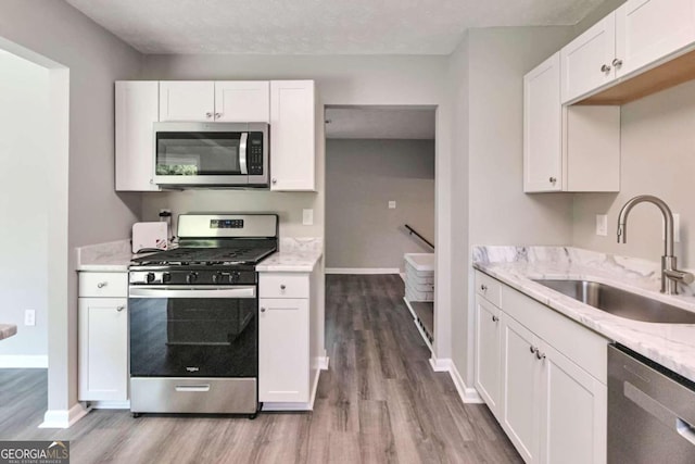 kitchen featuring light hardwood / wood-style flooring, sink, white cabinetry, light stone countertops, and stainless steel appliances