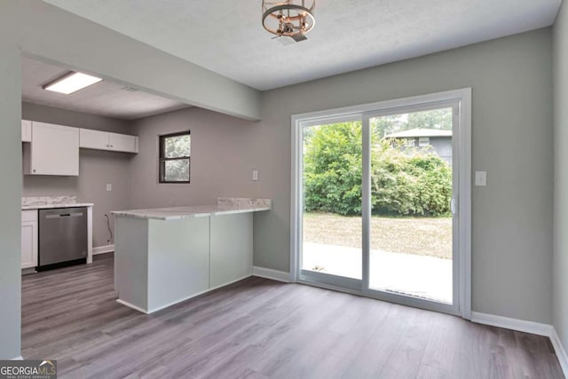 kitchen with kitchen peninsula, white cabinets, stainless steel dishwasher, and light hardwood / wood-style flooring