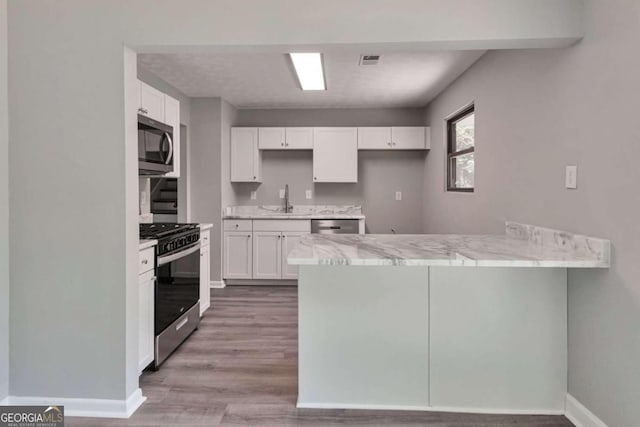 kitchen with kitchen peninsula, light hardwood / wood-style flooring, appliances with stainless steel finishes, sink, and white cabinets