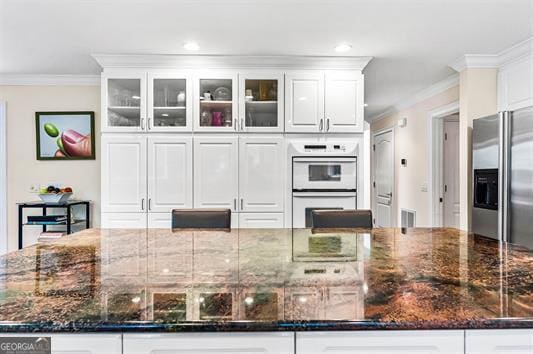 kitchen with white cabinetry, dark stone countertops, stainless steel refrigerator with ice dispenser, and white double oven