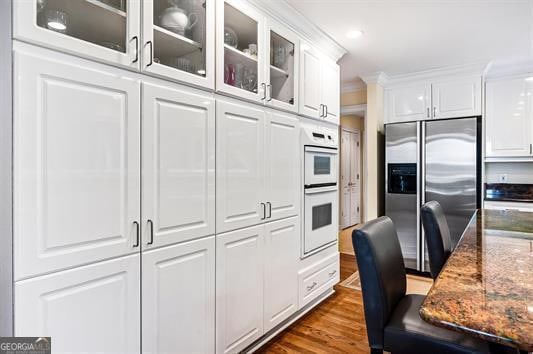 kitchen with stone counters, white double oven, stainless steel fridge with ice dispenser, white cabinetry, and wood-type flooring