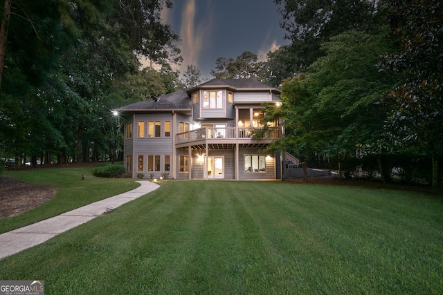 back of house at dusk with a wooden deck, roof with shingles, and a yard