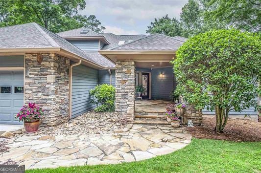 view of exterior entry featuring an attached garage, stone siding, and roof with shingles