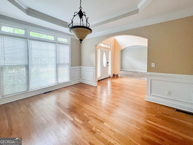 spare room featuring light hardwood / wood-style floors, crown molding, and a raised ceiling