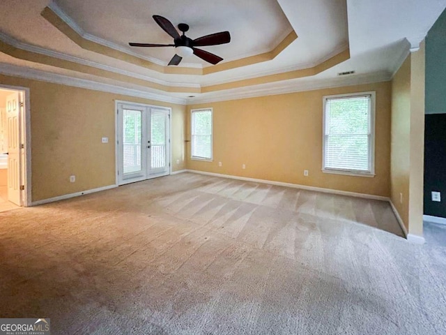 carpeted empty room with ceiling fan, french doors, a tray ceiling, and a wealth of natural light