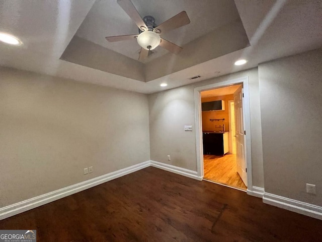 empty room featuring wood-type flooring, a raised ceiling, and ceiling fan