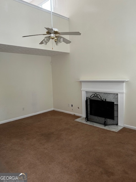 unfurnished living room featuring carpet flooring, ceiling fan, a towering ceiling, and a high end fireplace